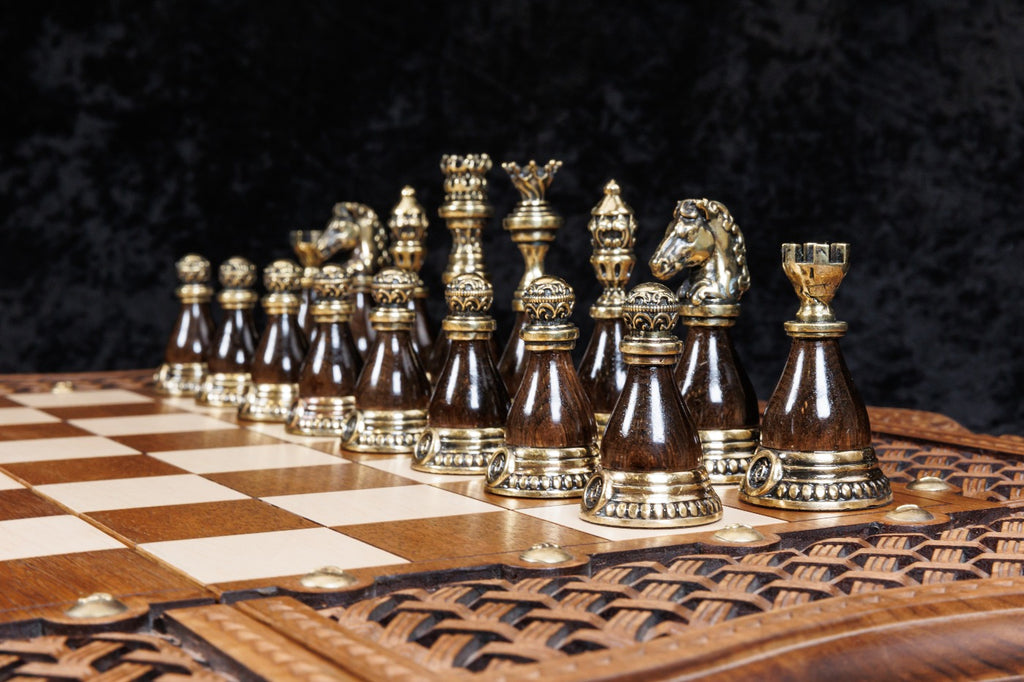 Bronze king, queen, bishop, knight and rook on dark bases on the chessboard, close-up