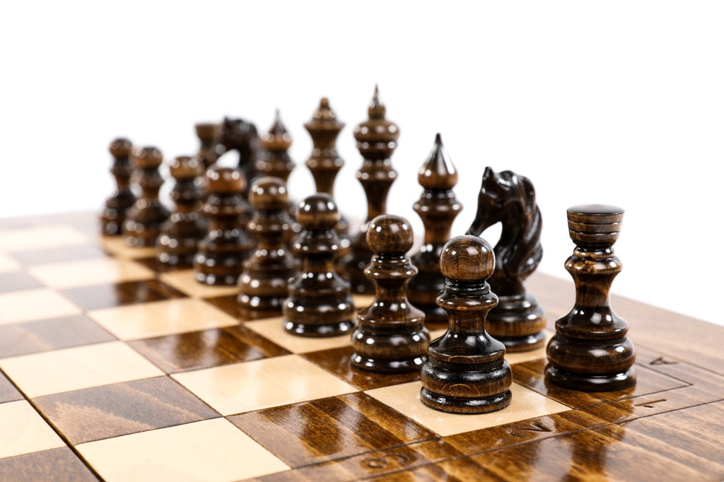 Dark hand-carved chess pieces on the large wooden chess board