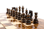 Dark hand-carved chess pieces on the large wooden chess board