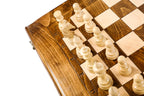 Light hand-carved chess pieces on the beech and walnut squares beside the carved letters