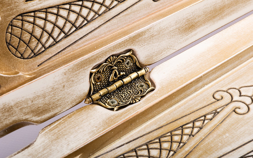 Ornate cast-bronze hinge on the white and gold backgammon board with lattice carving beside it