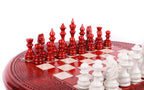 Red hand-carved chess pieces facing white pieces on the round painted chess board