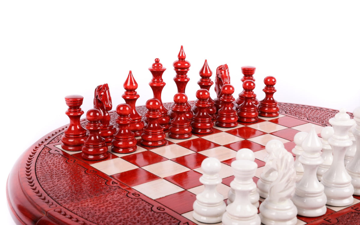 Red hand-carved chess pieces facing white pieces on the round painted chess board