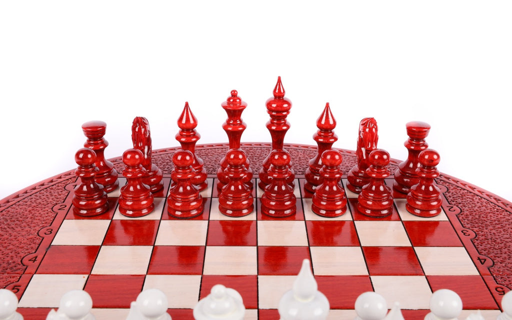 Red hand-carved chess pieces on the round board, white pieces in the foreground