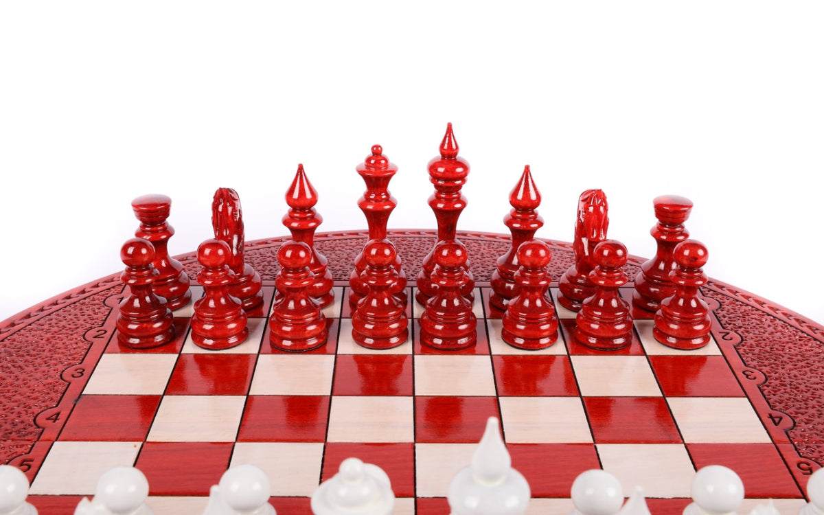 Red hand-carved chess pieces on the round board, white pieces in the foreground