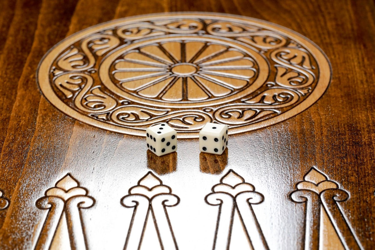Close-up of a carved spoked wheel in a scrolled ring inside the board, with a dice set