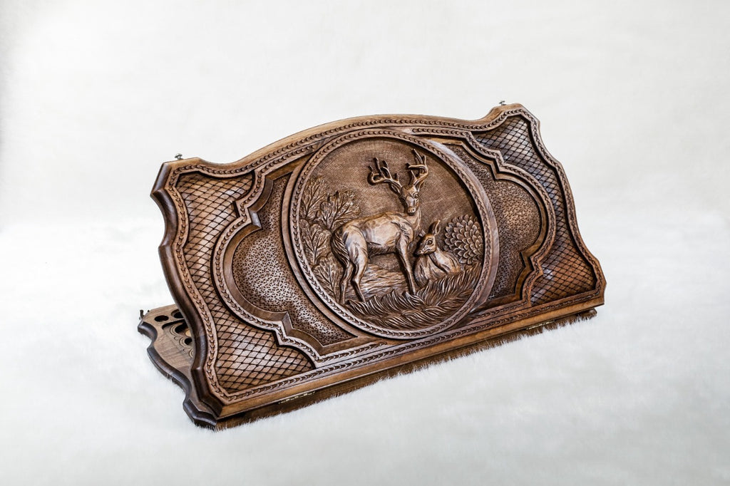 Closed backgammon board on edge, a stag with raised antlers and a doe resting in the grass