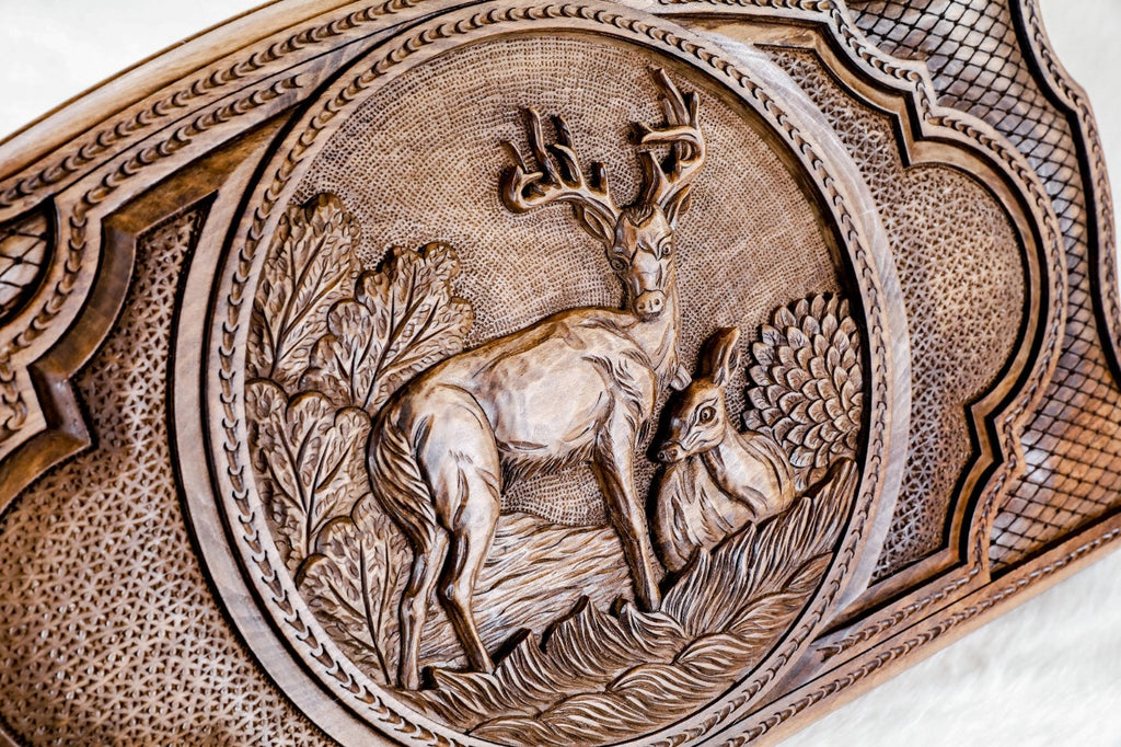 Close-up of the carved stag and doe among leafy trees, the antlers standing clear of the ground